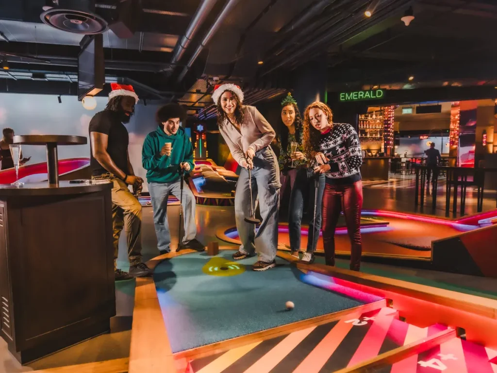 Friends mini golfing at Puttshack in festive Christmas clothing