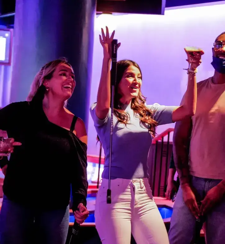 a woman raising her hands one with a putt in it and the other a cocktail