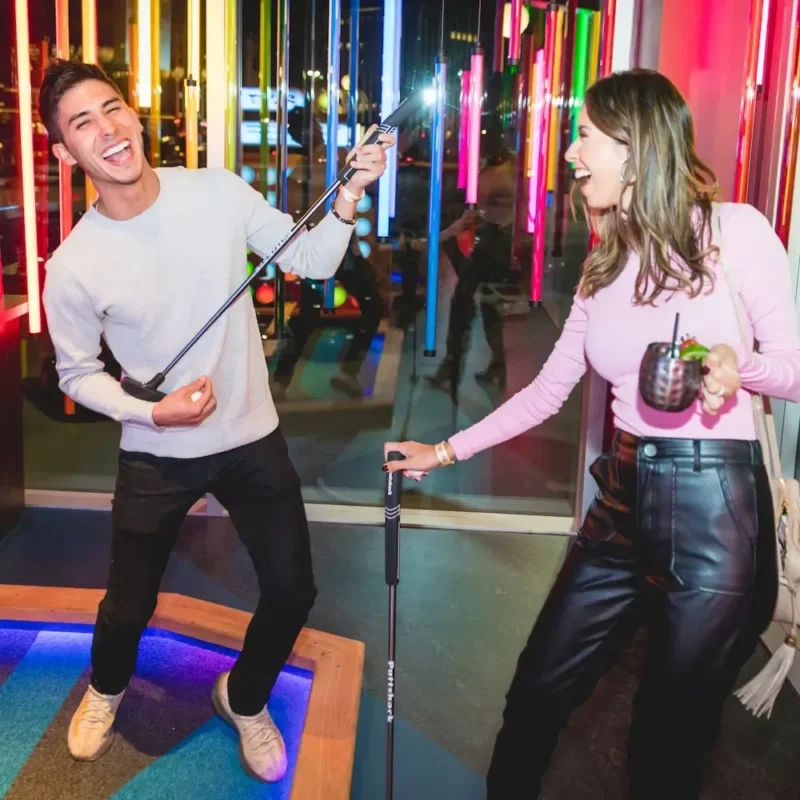 A happy man holding his putt like a guitar and a woman holding a drink and putt