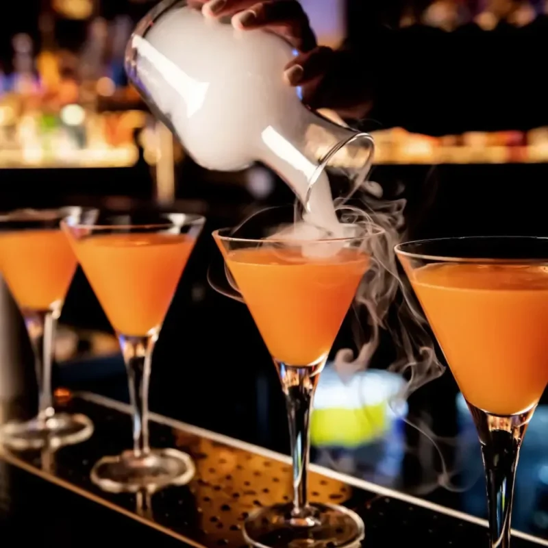 orange cocktails in a martini glass with a someone pouring smoke over one of them