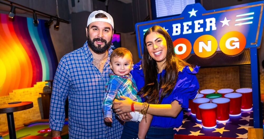 Dad and Mom holding their baby in front of the Beer Pong hole